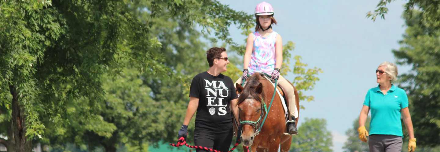 A young girl, accompanied by two adults, is shown riding a horse.